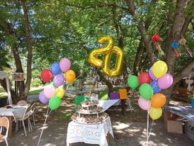Na staole stoją piętrowo ułożone babeczki, nad nimi wisi balonowa liczba 20, a obok fruwają kolorowe balony