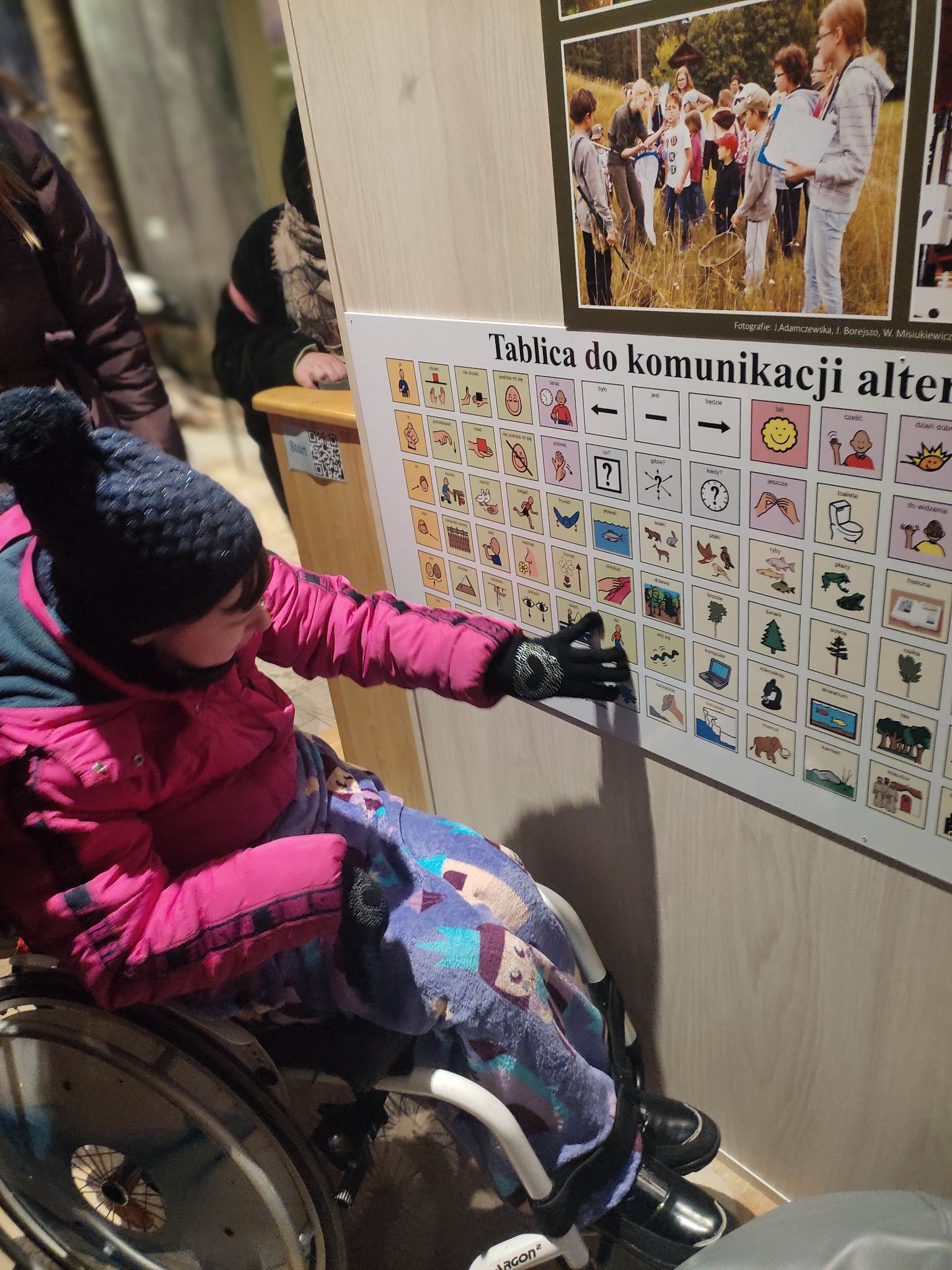 Tablica do komunikacji alternatywnej Kobieta na wózku inwalidzkim wskazuje na jeden z obrazków na tablicy do komunikacji alternatywnej.