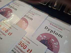 Pokaż zdjęcie: Stos dyplomów i kart z informacją o nagrodach pieniężnych w wysokości 300 zł dla laureatów regionalnego etapu XXII edycji Konkursu Plastycznego "Sztuka Osób Niepełnosprawnych"