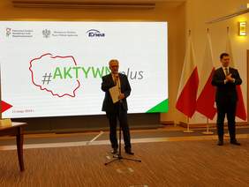 Pokaż zdjęcie: przemawiający mężczyzna, w tle ekran z napisem aktywni plus
