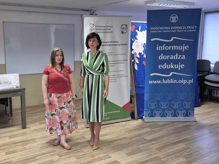 Pokaż zdjęcie: Do pamiątkowej fotografii pozują dwie prelegentki na tle rollupów z logo CIDON oraz Inspekcji Pracy.