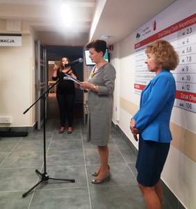 Pokaż zdjęcie: Prezydent m. st. Warszawy wraz z Dyrektorem Urzędu stoją przy mikrofonie, w tle widać tłumacza języka migowego