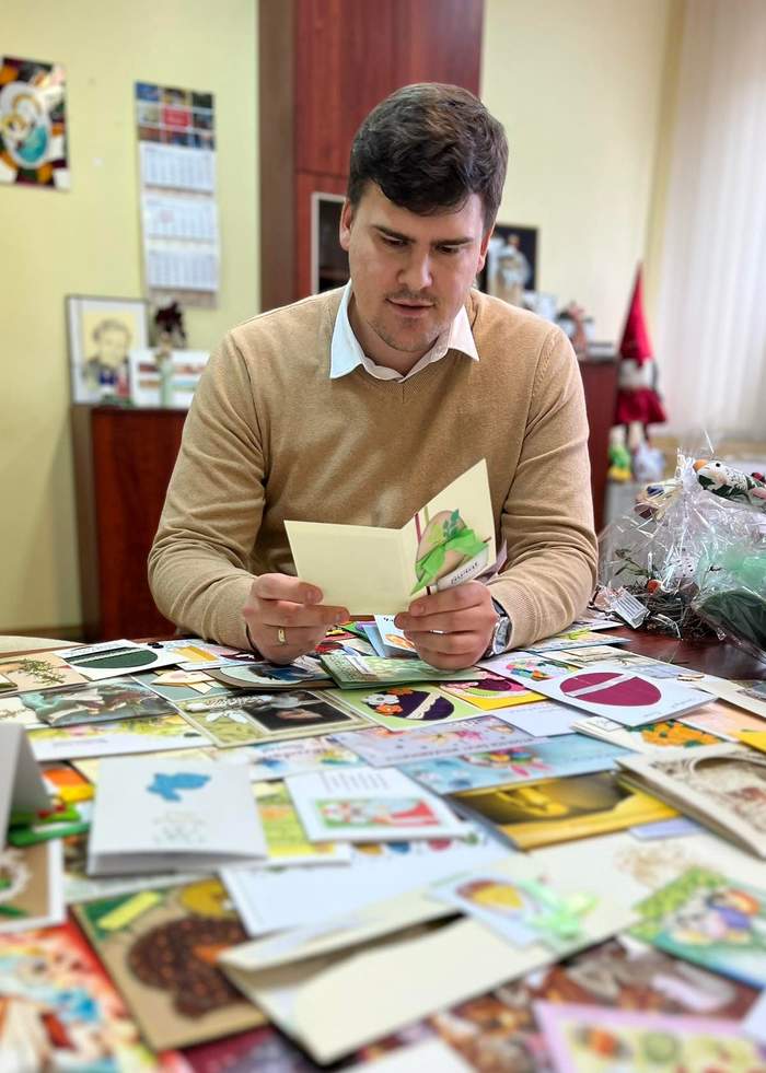 Pokaż zdjęcie: Na zdjęciu znajduje się mężczyzna, który siedzi przy stole pełnym kartek świątecznych i przegląda je