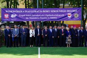 Pokaż zdjęcie: Zebrani przedstawiciele władz pod banerem z informacją o Wojewódzkiej Inauguracji Roku Szkolnego 2022/2023 z logami Województwa Warmińsko-Mazurskiego, Wojewódzkiego Kuratorium Oświaty, Starostwa Nidzickiego, ZSZiO w Nidzicy. 
