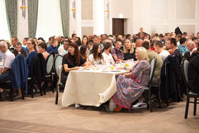 Duża, przestronna sala, liczni goście siedzą przy stołach 