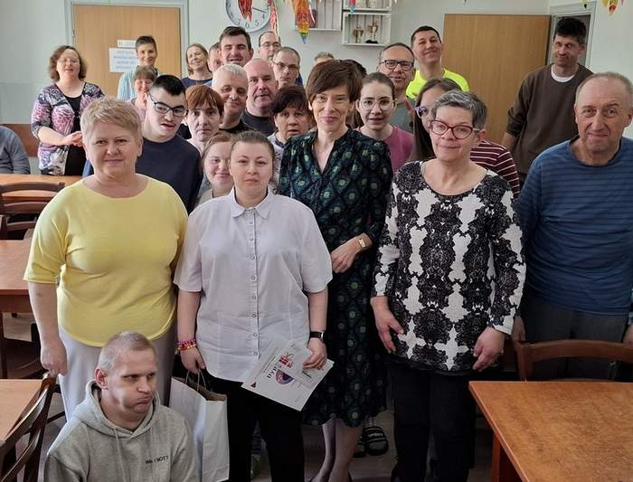 Pokaż zdjęcie: Grupa uczestników Środowiskowego Domu Samopomocy w Krotoszynie pozuje do wspólnego zdjęcia. Większość osób stoi w rzędach, a jedna osoba siedzi na przodzie.