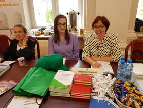 trzy kobiety siedzą przy stole na którym leżą różne materiały informacyjne i promocyjne