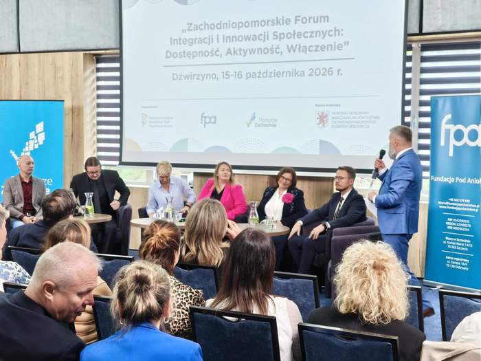 Panel dyskusyjny podczas Zachodniopomorskiego Forum Integracji i Innowacji Społecznych „Dostępność, Aktywność, Włączenie”, które odbyło się 15–16 października 2026 r. w Dźwirzynie. Paneliści siedzą na scenie, a prowadzący z mikrofonem zwraca się do uczestników zgromadzonych na sali. W tle widoczne są ekran z nazwą wydarzenia i banery organizatorów.