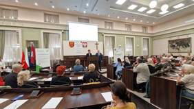 Pokaż zdjęcie: Wystąpienie na mównicy Prezydent Miasta Kielce oraz Dyrektora Oddziału Świętokrzyskiego PFRON podczas spotkania z seniorami. Na zdjęciu sala obrad urzędu miasta, na niej zaproszeni goście.