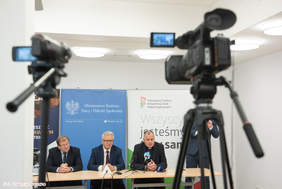 Pokaż zdjęcie: Trzech mężczyzn siedzących za stołem konferencyjnym odpowiada na pytania dziennikarzy