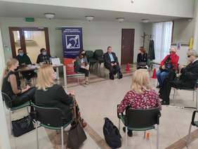 Pokaż zdjęcie: w pomieszczeniu 10 osób siedzi w kole z tyłu stoi baner z napisem strefa objęta pętlą indukcyjną