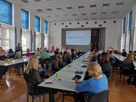 Pokaż zdjęcie: Zdjęcie sali konferencyjnej, przy stołach siedzą uczestnicy konferencji, patrzą w kierunku wyświetlanej prezentacji