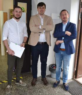 Pokaż zdjęcie: 3 mężczyzn stoi w holu szkoły, uśmiechają się