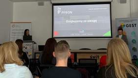 Pokaż zdjęcie: Dwie kobiety stoją po obu stronach dużego ekranu, na którym wyświetlone jest: logo PFRON, nazwa Oddział Wielkopolski PFRON oraz sformułowanie „Dziękujemy za uwagę”. Na sali widoczna jest grupa sześciu osób, która przysłuchuje się wystąpieniu.