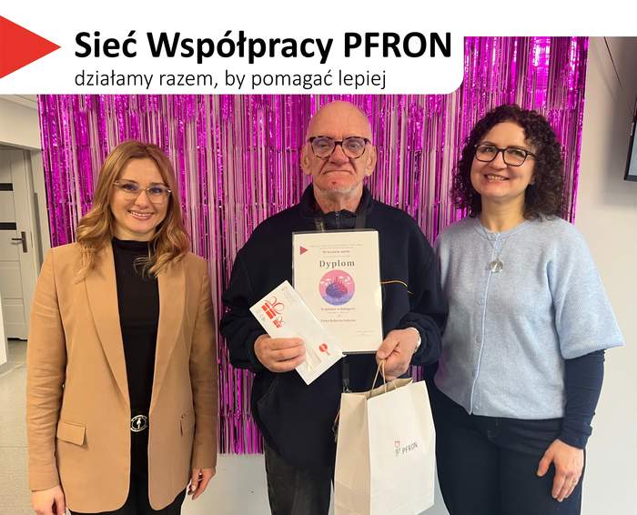 Pokaż zdjęcie: Na górze, na białym tle, widoczny jest czerwony, trójkątny element. Obok znajduje się tekst: 'Sieć Współpracy PFRON', a poniżej napis: 'działamy razem, by pomagać lepiej'. W centrum stoi mężczyzna trzymający dyplom oraz białą torbę z logo PFRON. Po lewej towarzyszy mu kobieta o długich blond włosach w okularach. Po prawej stoi kobieta z ciemnymi, kręconymi włosami w okularach, ubrana w jasnoniebieski sweter.