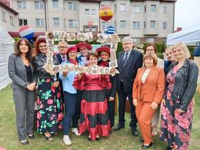 Pokaż zdjęcie: Grupa osób pozuje do zdjęcia. Niektórzy są przebrani w stroje różnych europejskich narodowości. W tle są balony - europejskie flagi. 