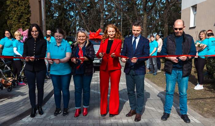 Pokaż zdjęcie: Grupa osób przecina wstęgę w kolorze czerwonym, a za niminowe auto dofinansowane z PFRON