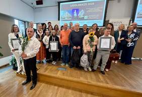 Pokaż zdjęcie: Grupa Laureatów pozuje do zdjęcia na scenie. Trzymają kwiaty, dyplomy i statuetki.