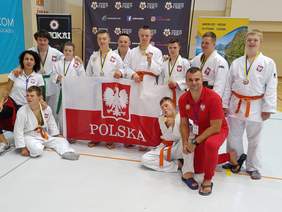 Pokaż zdjęcie: 10 zawodników z trenerami i rozwiniętą flagą Polski