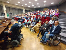Sala konferencyjna, układ krzeseł jak kinie w rzędach wznoszących się coraz wyżej, kilkudziesięciu uczestników