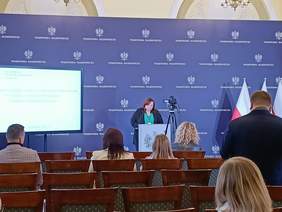 Pokaż zdjęcie: Na scenie, za mównicą przemawia Dyrektor Wydziału do Spraw Osób Niepełnosprawnych Marzena Tazbir-Kowalczyk