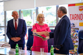 Pokaż zdjęcie: Przekazanie umowy w Starostwie Powiatowym. Od lewej: wicestarosta Jacek Hudyma, dyrektor Marta Mordarska oraz starosta Roman Łucarz. Dyrektor przekazuje staroście teczkę z dokumentami.