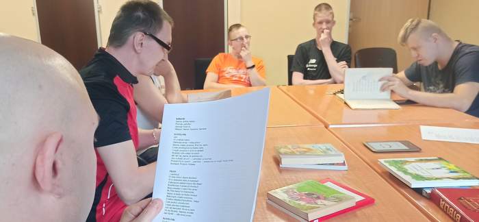 Pokaż zdjęcie: sześciu młodych mężczyzn siedzi przy stole oglądają książki czytają lub słuchają