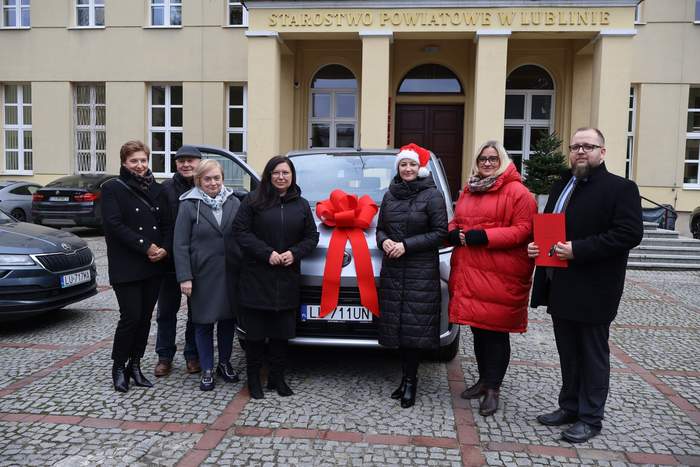 Pokaż zdjęcie: Przed samochodem udekorowanym kokardą pozuje sześć osób do pamiątkowego zdjęcia.