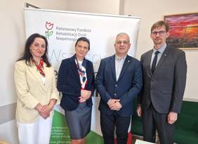 Pokaż zdjęcie: Dwie kobiety i dwóch mężczyzn pozują do zdjęcia na tle logo PFRON.