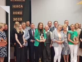 Pokaż zdjęcie: Na zdjęciu stoi grupa osób w półkolu. Wszyscy się uśmiechają do zdjęcia.