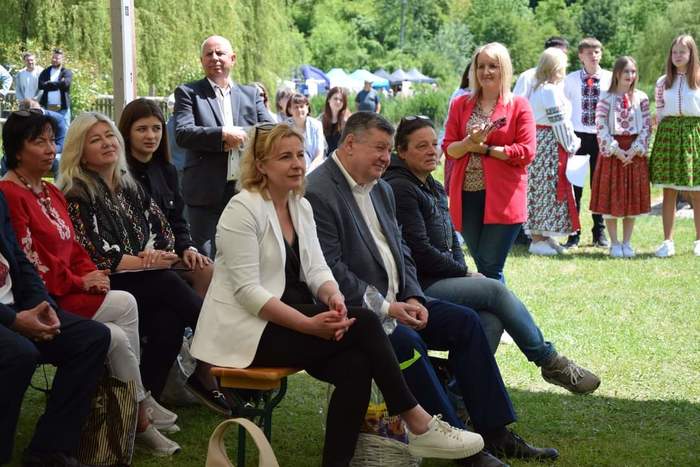 Pokaż zdjęcie: Pod namiotem, na ławkach siedzą zaproszeni goście na obchody Powiatowego Dnia Pieczy Zastępczej.