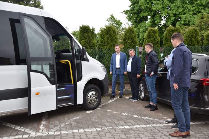 Pokaż zdjęcie: Połowa białego busa do transportu osób niepełnosprawnych, obok stoi pięciu panów odświętnie ubranych.  