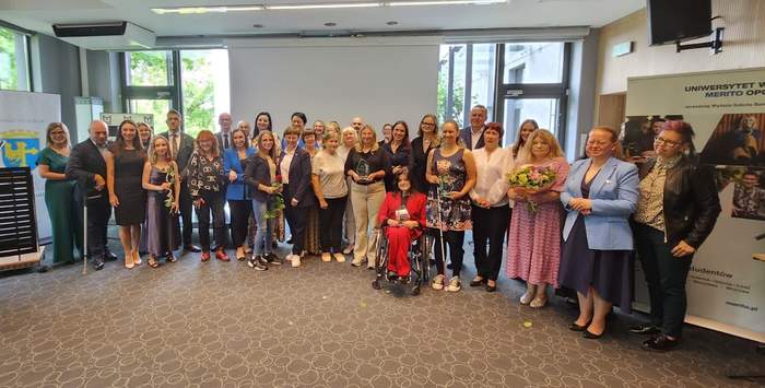 Pokaż zdjęcie: Grupa osób zwrócona w jednym kierunku pozująca do fotografii pamiątkowej. W tle ekran oraz okna sali konferencyjnej.