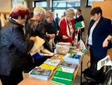Stoisko informacyjne PFRON, seniorzy sięgają po ulotki i informatory ułożone na stoliku.