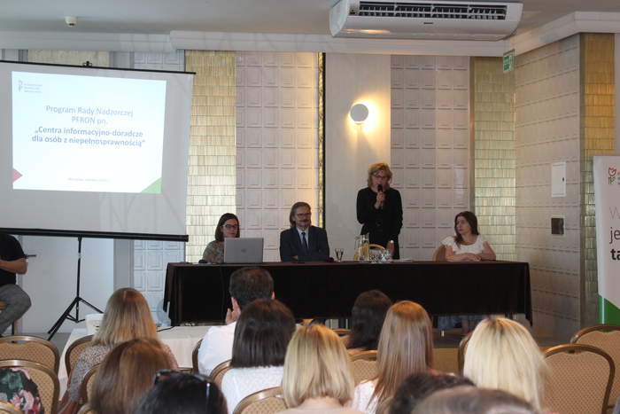 Pokaż zdjęcie: W sali konferencyjnej za stołem prezydialnym siedzą cztery osoby, trzy kobiety i jeden mężczyzna, po lewej stronie ekran z prezentacją