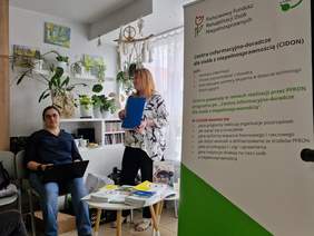 Pokaż zdjęcie: dwie przedstawicielki PFRON obok plakatu z napisem „Centra informacyjno-doradcze dla osób z niepełnosprawnością ”CIDON”