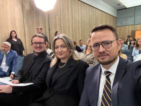 Uczestnicy Zachodniopomorskiego Forum Integracji i Innowacji Społecznych „Dostępność, Aktywność, Włączenie” podczas wydarzenia w Dźwirzynie. Trzy osoby siedzące w pierwszym rzędzie pozują do wspólnego zdjęcia na tle pozostałych uczestników spotkania.