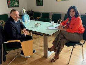 Pokaż zdjęcie: Sala konferencyjna. Przy szklanym stole siedzą kobieta i mężczyzna. Rozmawiają, na stole leżą dokumenty.