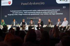 Pokaż zdjęcie: Na scenie na krzesełkach siedzi ośmiu panelistów.