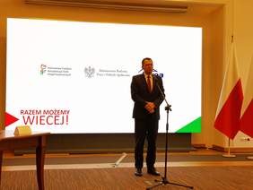 Pokaż zdjęcie: Przemawia mężczyzna w garniturze, w tle ekran z napisem: Razem możemy więcej. 