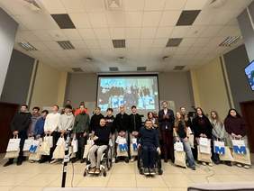 Grupa osób, młodzież i dorośli, część stoi, dwóch mężczyzn siedzi na wózkach