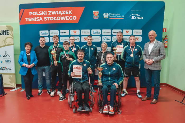 Pokaż zdjęcie: Sportowcy z niepełnosprawnościami, w tym na wózkach, ubrani w stroje sportowe na pamiątkowym zdjęciu z Dyrektor Oddzialu PFRON