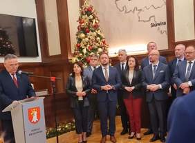 Pokaż zdjęcie: Uczestnicy Spotkania Opłatkowego w siedzibie Starostwa Powiatowego w Krakowie. Przy mównicy przemawia mężczyzna, uczestnicy słuchają wypowiedzi. Wszyscy są elegancko ubrani.