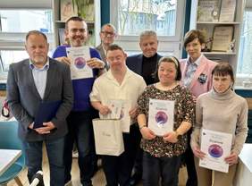 Pokaż zdjęcie: Zdjęcie grupowe ośmiu osób, z których część trzyma pamiątkowe dyplomy laureatów i uczestników XXII edycji wojewódzkiego etapu Konkursu Plastycznego „Sztuka Osób Niepełnosprawnych”.
