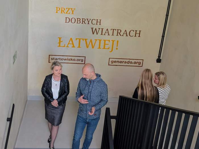 Pokaż zdjęcie: Po schodach w budynku idą kobiety i męzczyna i rozmawiają
