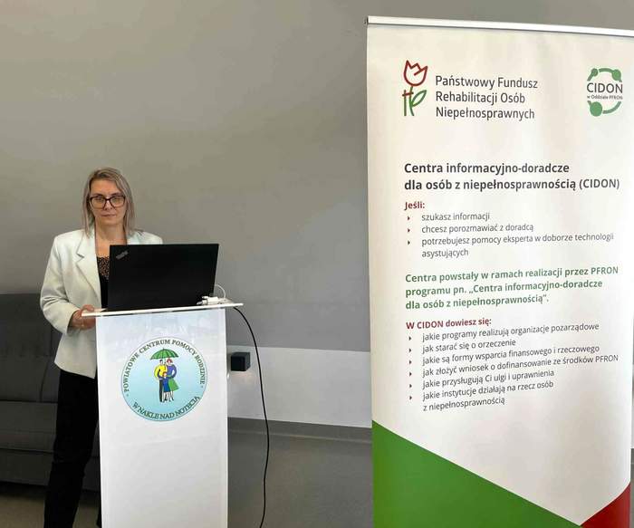 Na obrazku: po lewej stronie stoi prelegentka - pracownik Kujawsko-Pomorskiego Oddziału PFRON, a obok niej widać baner z logo CIDON PFRON