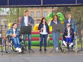 Na scenie 6 osób w tym 2 na wózkach inwalidzkich, śpiewają