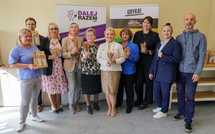 Pokaż zdjęcie: Grupa osób trzyma w rękach paluszki, które powstają w placówce Fundacji Generado, o czym informują rollupy w tle