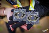 Zbliżenie na dwa medale V edycji Biegu w Ciemno w Szczecinie, trzymane na dłoni. Na medalach widnieje motyw oka, napis „Bieg w Ciemno” oraz wypukłe oznaczenia w alfabecie Braille’a.