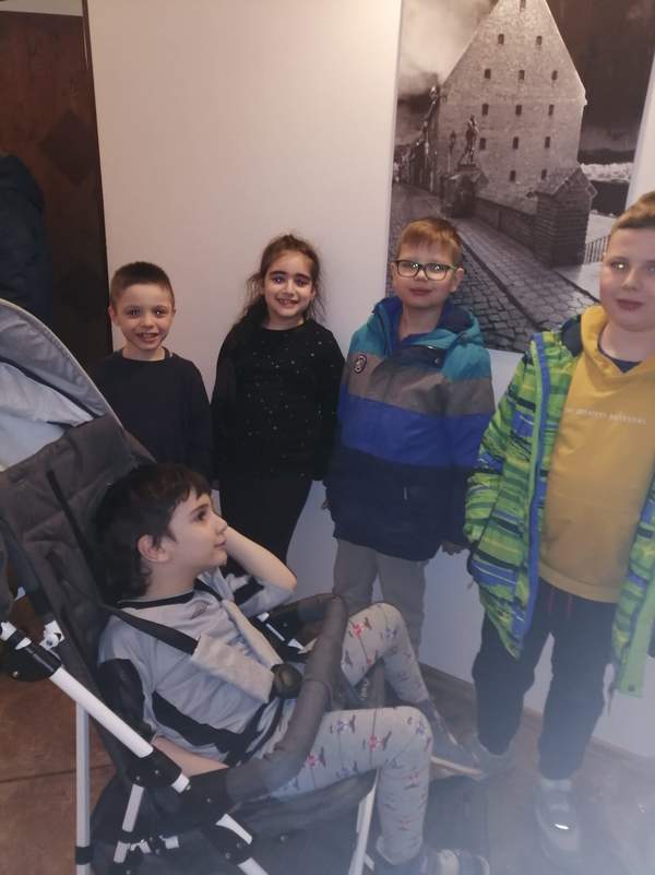 Czworo dzieci stoi pod ścianą , a jedno siedzi na wózku